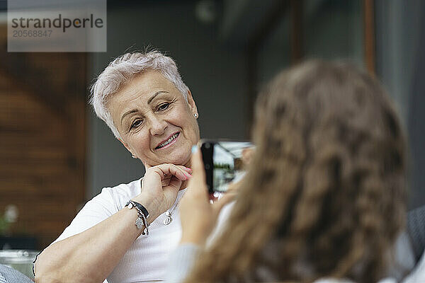 Granddaughter photographing grandmother through smart phone at patio