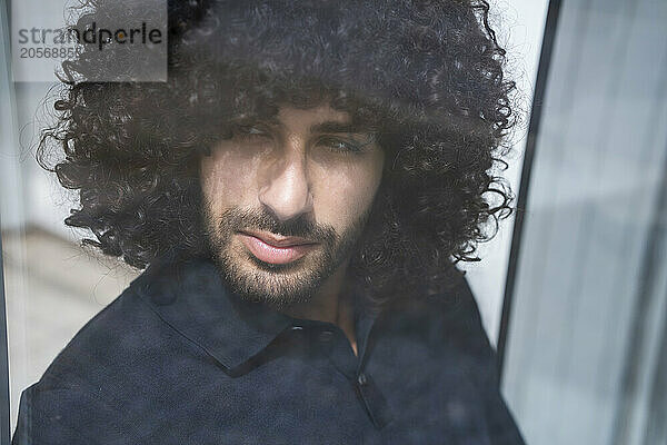 Confident curly haired businessman looking out through window