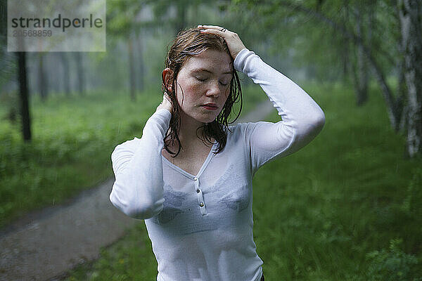 Young woman with eyes closed and hand in hair at forest