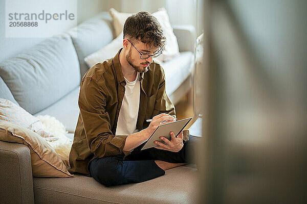 Young man using tablet PC sitting on sofa at home