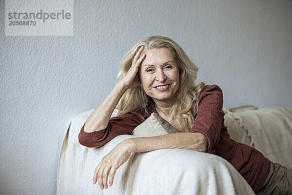 Smiling blond senior woman relaxing on sofa in living room at home