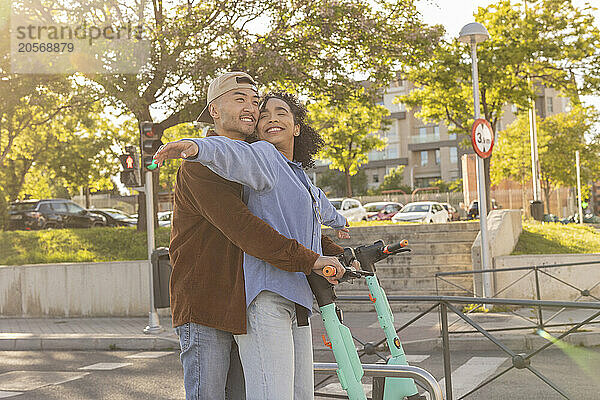 Carefree multiracial couple standing with electric push scooter at park