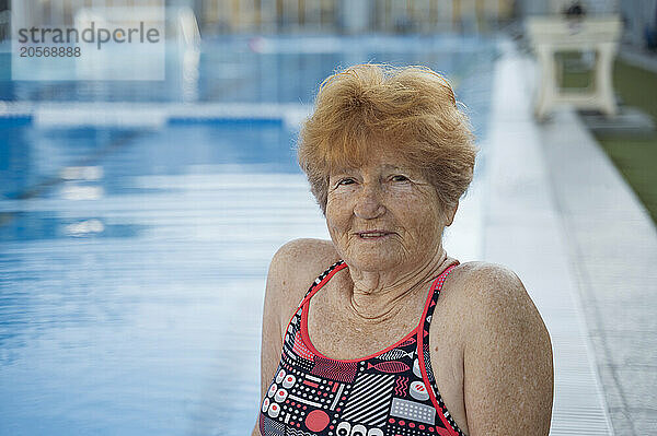 Blond hair senior woman with freckles sitting near swimming pool