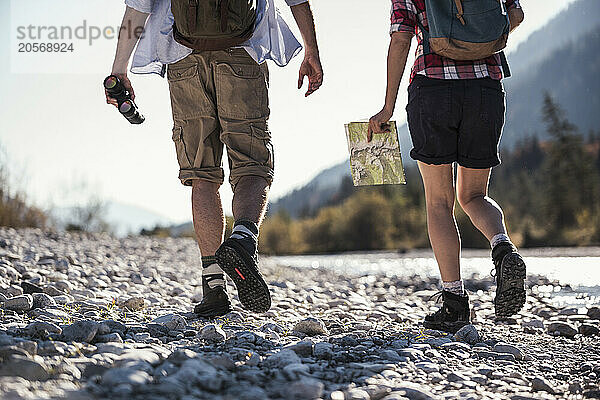 Friends with map and binoculars walking on pebbles