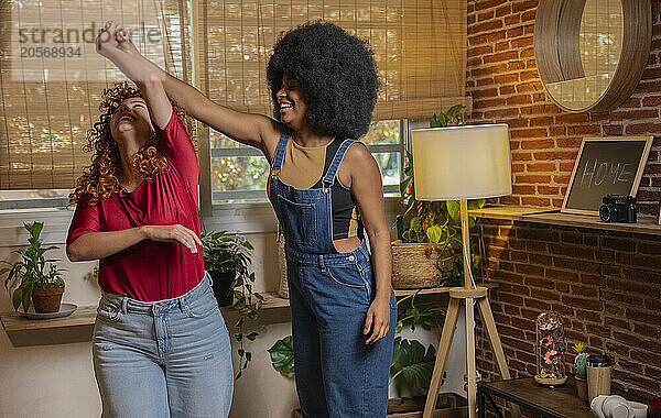 Happy Afro woman dancing with redhead friend at home