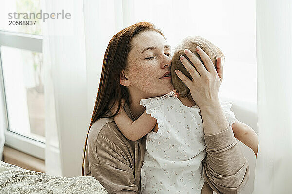 Woman with eyes closed hugging daughter at home