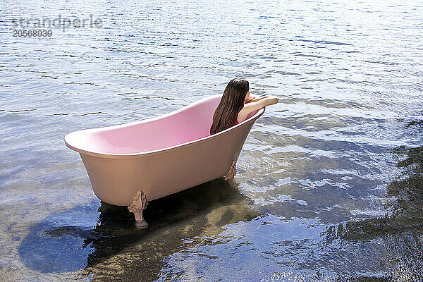 Girl sitting inside pink colored bathtub in lake