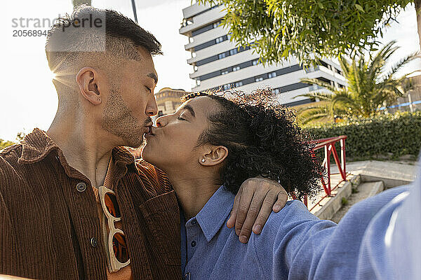 Multiracial couple kissing and taking selfie at park