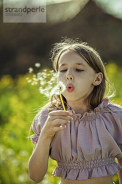 Girl blowing on dandelion flower at field on sunny day