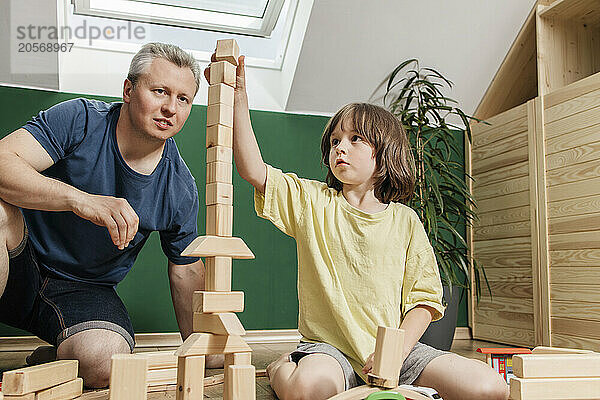 Focused boy stacking toy block with father at home