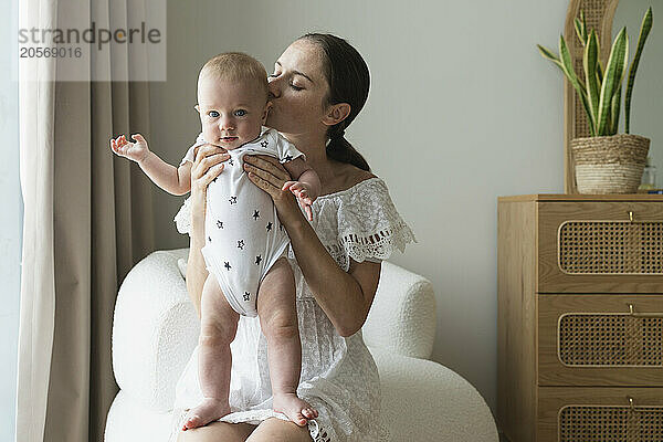 Mother kissing son and sitting on chair at home