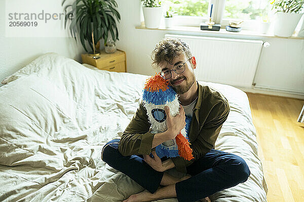 Young man hugging rocketship shaped pinata sitting on bed at home