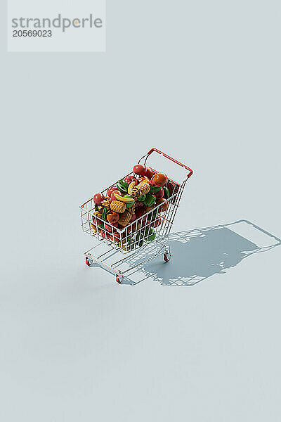 Shopping cart filled with artificial fruits and vegetables over blue background