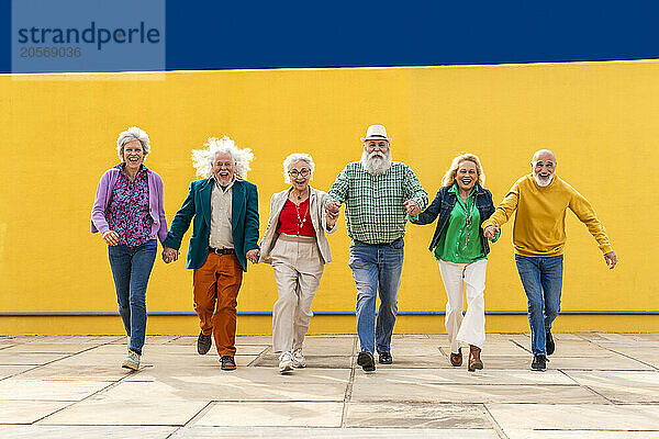 Elderly carefree friends holding hands and running on footpath