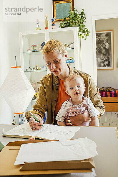 Woman writing in diary sitting with daughter at home