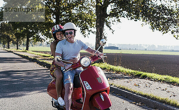 Carefree young couple riding motor scooter at country road