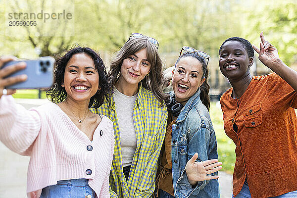 Smiling woman taking selfie with multiracial friends through smart phone