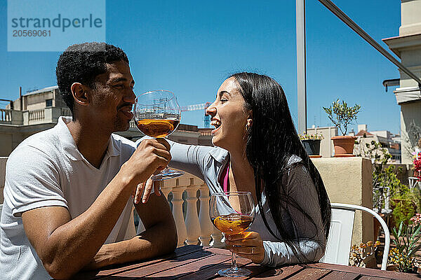 Cheerful young couple enjoying drink at building terrace on sunny day