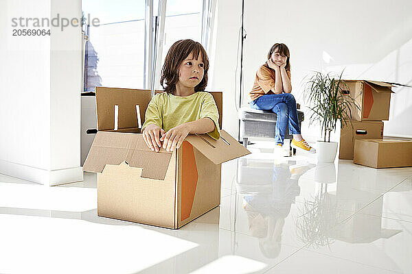 Boy in cardboard box with sister sitting at new house