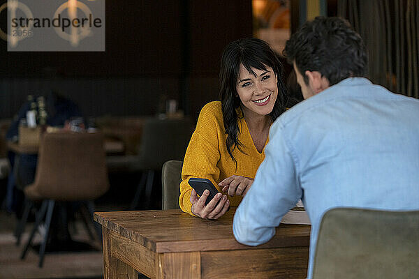 Happy businesswoman discussing over smart phone with businessman in cafe