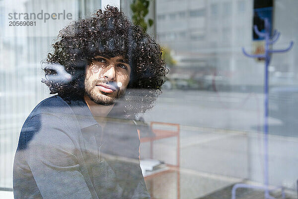 Thoughtful businessman with curly hair looking out through window