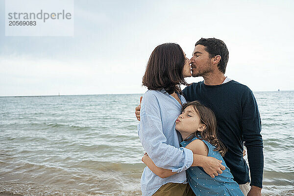 Man and woman kissing each other with daughter at beach