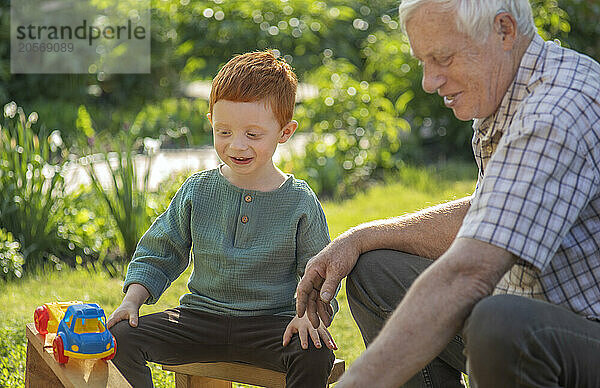 Happy grandfather and grandson playing with toy truck on sunny day