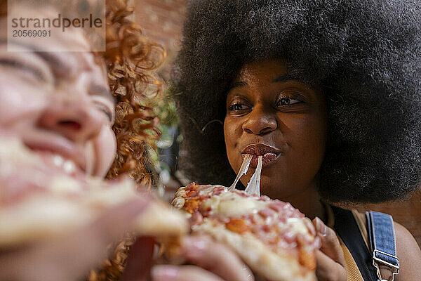 Afro woman eating slice of pizza with roommate