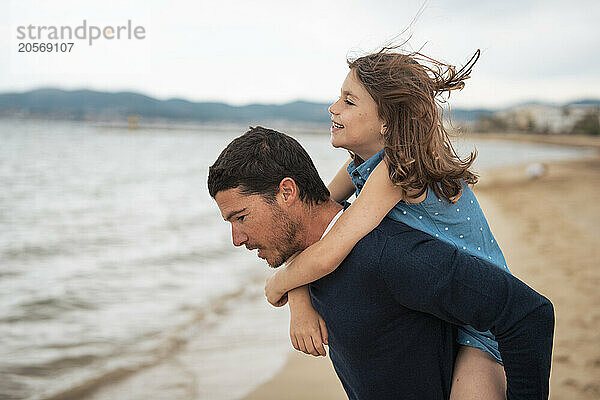 Father giving piggyback ride to daughter at beach