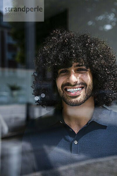 Happy businessman with curly hair looking out through window