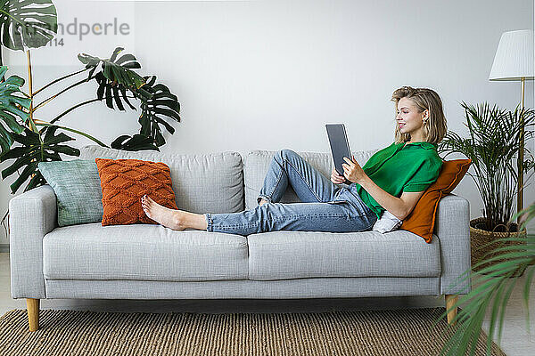 Young woman using tablet PC reclining on sofa at home