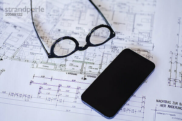 Eyeglasses and smart phone on blueprint at desk in office