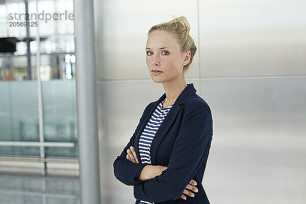 Confident young businesswoman standing with arms crossed in airport lobby