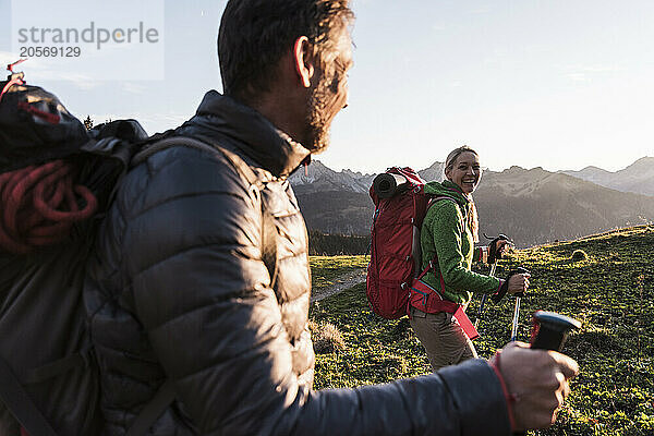 Cheerful woman with backpack and hiking pole walking with boyfriend on mountain of Tyrol