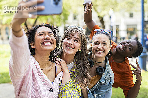 Cheerful woman taking selfie with friends through smart phone