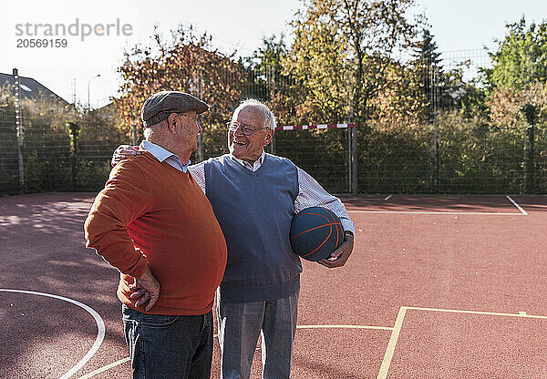 Smiling senior friends playing basketball at court