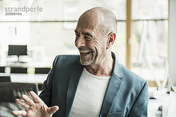 Happy mature businessman with shaved head gesturing at office