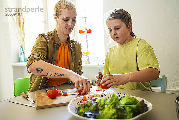 Mother and son chopping tomatoes sitting at dining table