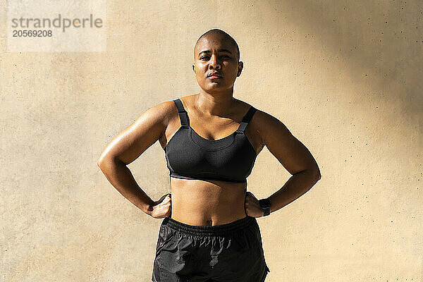 Confident muscular woman standing with arms akimbo in front of wall