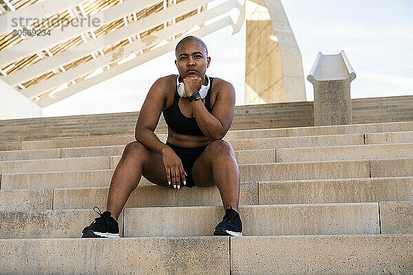 Confident muscular woman wearing headphones sitting on steps