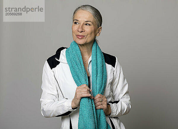 Smiling senior woman with turquoise towel looking away against gray background