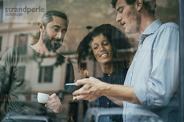 Colleagues using smartphone and sharing thoughts with each other at cafe