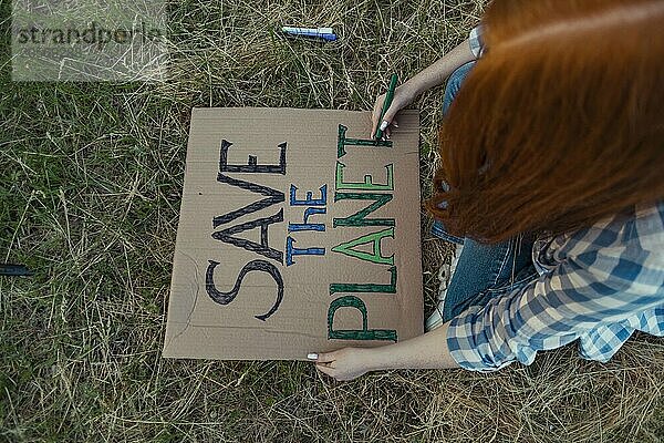 Teenage girl coloring alphabets of protest banner at public park