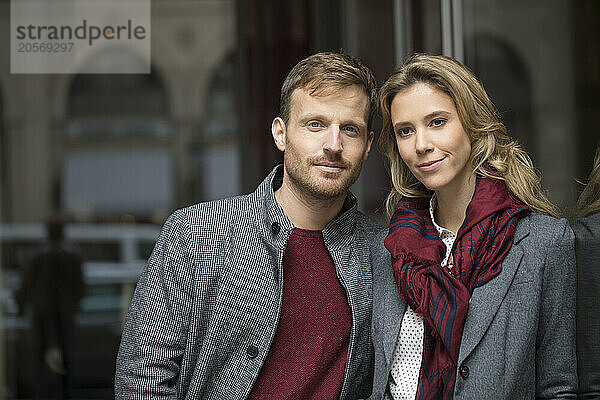 Boyfriend and girlfriend wearing warm clothes and leaning on glass wall