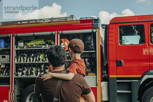 Father carrying son in front of fire truck