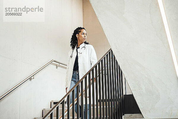 Confident female doctor moving down on staircase at hospital