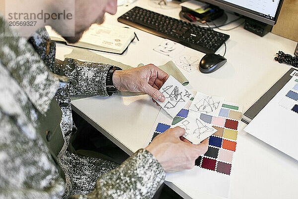 Fashion designer comparing designs at desk in workshop