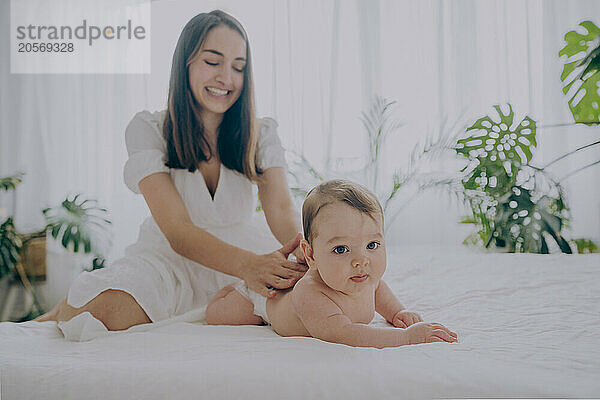 Smiling mother massaging baby boy lying on bed at home