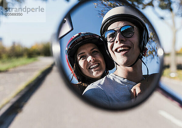 Happy young couple wearing safety helmets seen in scooter mirror