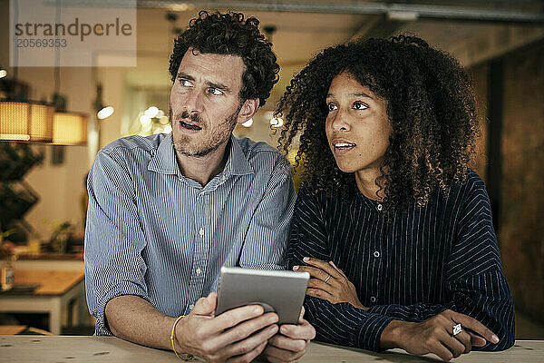 Businessman holding tablet PC sitting with colleague in cafe